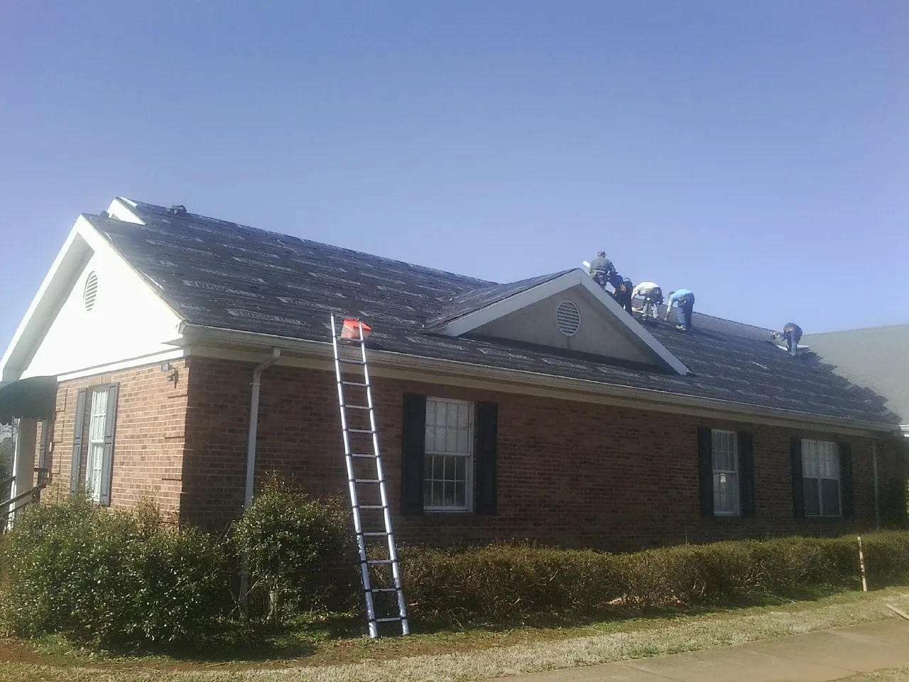 Crew tearing shingles off a brick ranch roof with a ladder set — Emergency Roof Repair work by our crew in Depew
