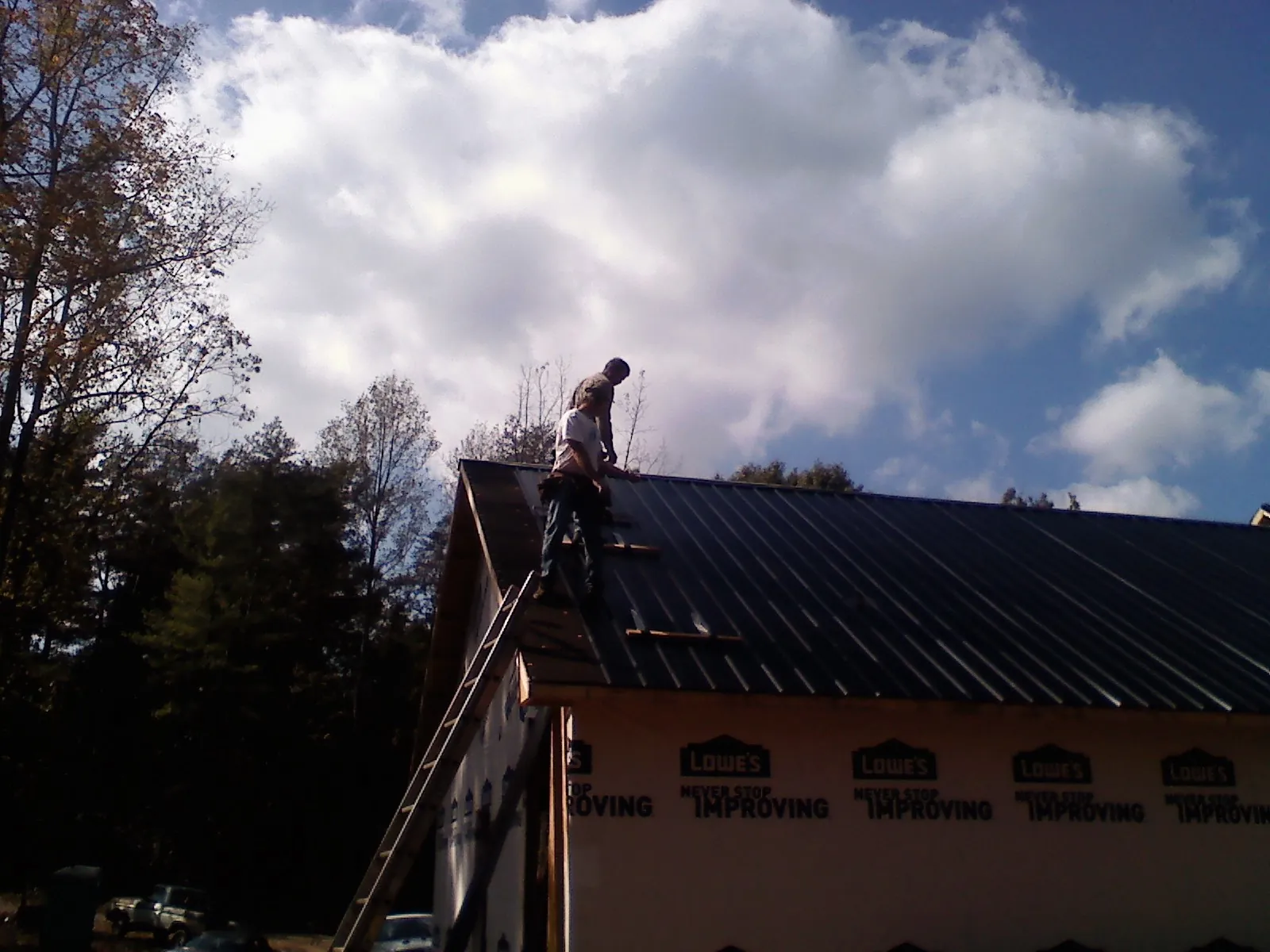 Roofer fastening dark metal panels high against a cloudy sky, from a Roof Inspection job in Depew