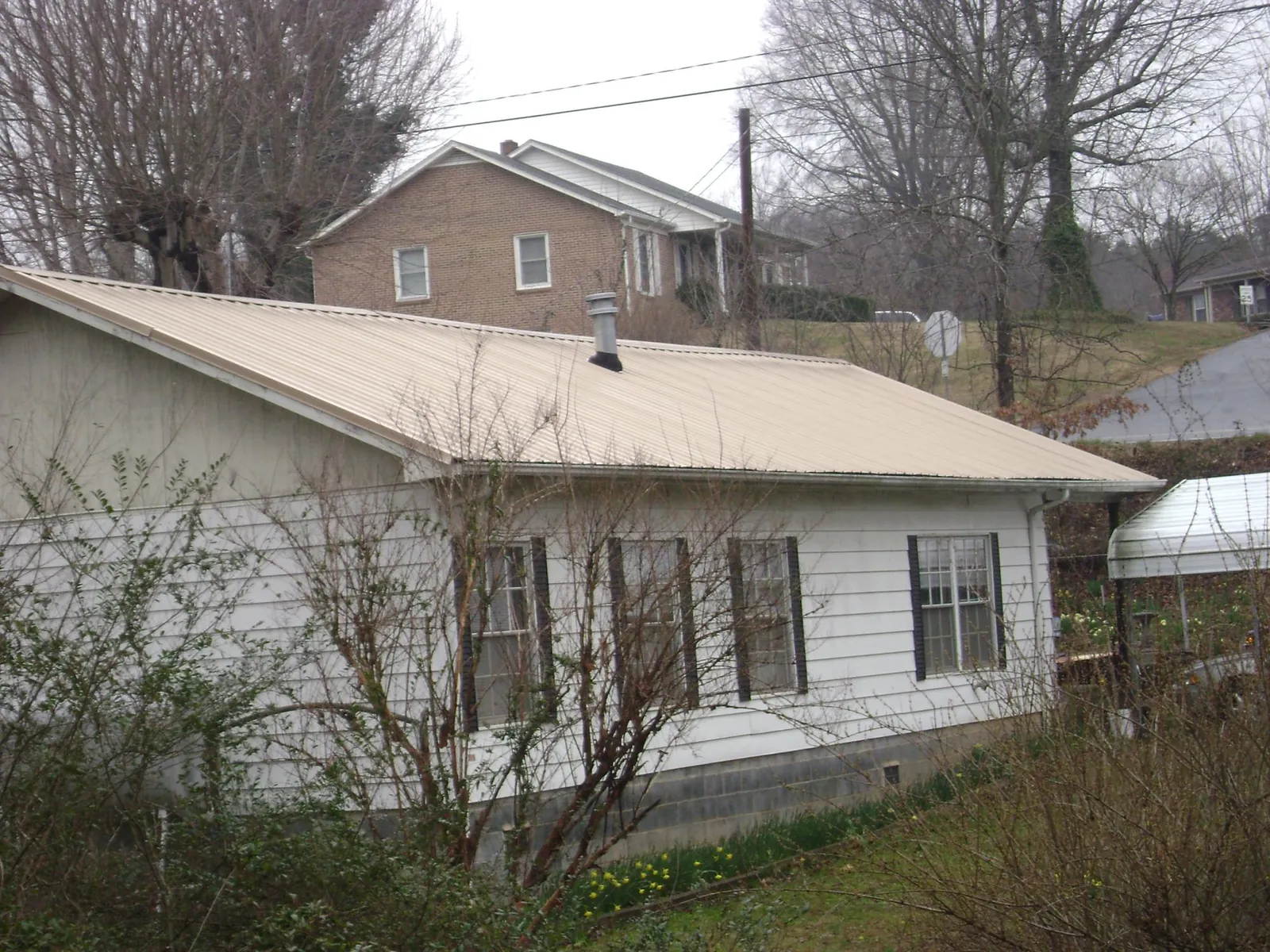Tan metal roof on a white sided house set into a hillside — Commercial Roofing by Roofing Brothers in Depew